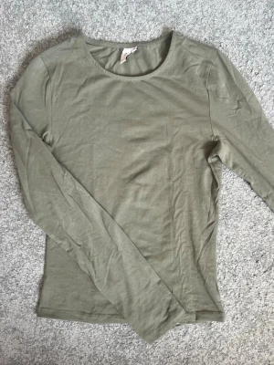 Olivgrön långärmad topp - En enkel och stilren olivgrön långärmad topp med rund halsringning. Tillverkad i mjuk bomull som känns skön mot huden. Perfekt att matcha med jeans eller kjol för en clean look.