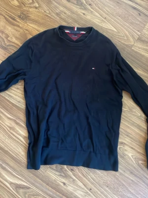 Svart tröja från Tommy Hilfiger - Snygg svart tröja från Tommy Hilfiger med rund halsringning och diskret logga på bröstet. Tröjan har långa ärmar och är tillverkad i ett mjukt material som passar perfekt till en clean och stilren look. Är XL men sitter mycket mer som L.