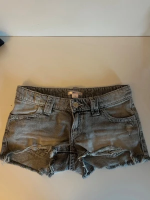 Gråa jeansshorts  - Snygga grå denimshorts från Gina med fransig kant och slitna detaljer. Shortsen har klassisk femficksdesign, bälteshällor och broderade bakfickor. Perfekta för varma dagar och en avslappnad stil.