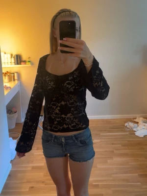 Svart spetsblus med snörning - Säljer en svart, transparent spetsblus med långa ärmar och snygg snörning framtill. Blusen har ett feminint mönster och en lätt croppad passform som ger en trendig look. Perfekt att styla med jeans eller kjol. Endast testad har två till spetstoppar och därför kommer den ej till användning tvättas innan den skickas 