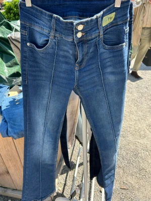 Blå jeans med låg midja och söm - Säljer ett par blå jeans med låg midja och dubbla knappar framtill. Jeansen har markerad söm längs benen, klassiska fem fickor och lätt tvättad look. Materialet är stretchigt denim för skön passform. Perfekta till en avslappnad stil.