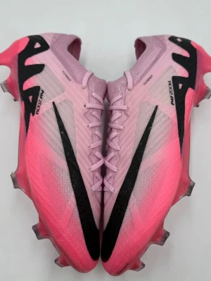 Nike rosa Mercurial fotbollsskor - Säljer ett par Nike Mercurial fotbollsskor i en snygg rosa färg med svarta detaljer och logga. Skorna har en strömlinjeformad design, snörning och taggiga dobbar för bra grepp på planen. Ovandelen är tillverkad i ett lätt syntetmaterial för optimal bollkontroll. Förhandlingsbart pris