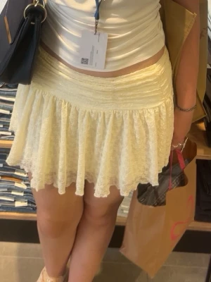 Ljusgul volangkjol i spets - Supersöt kort kjol i ljusgul spets med volang och bred midjeresår. Kjolen har en feminin och flowy passform som ger en romantisk vibe. Perfekt att styla med en enkel topp för en fräsch look.