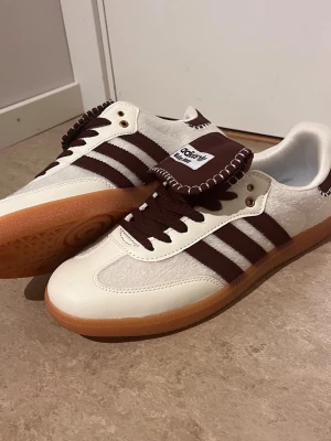 Adidas Wales Bonner vita sneakers - Säljer ett par Adidas Wales Bonner sneakers i vitt och brunt med klassiska tre ränder på sidan. Skorna har brun sula i gummi, bruna skosnören och detaljerad söm på plösen. Materialmix av mocka och läder ger en unik look.
