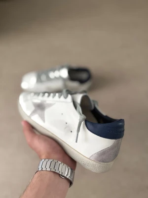 Golden Goose vita sneakers med stjärna - Snygga vita sneakers från Golden Goose med grå mockadetaljer, silverfärgad stjärna på sidan och mörkblå hälkappa. Kommer tyvärr inte med låda. 