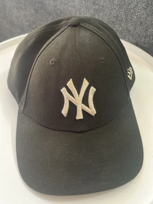 Svart New Era NY Yankees keps - Svart keps från New Era med klassisk New York Yankees-logga broderad framtill i vitt. Modellen är 9FORTY. Justerbar passform med böjd skärm och broderad New Era-logga på sidan.