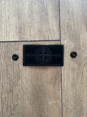 Stone Island Ghost Badge – Helt ny & Äkta - Säljer en exklusiv "Ghost Badge" från Stone Island. Helt ny och i perfekt skick. En eftertraktad detalj för den som vill uppgradera sin Stone Island-jacka eller samling. Passar perfekt för dig som gillar det stilrena, helt svarta "Ghost"-konceptet från Stone Island. 