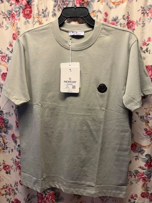  Moncler t-shirt i bomull - Snygg ljusgrå t-shirt från Moncler med klassisk passform och rund hals. T-shirten har korta ärmar och en diskret Moncler-logga på bröstet. Tillverkad i mjuk bomull som känns skön mot huden.