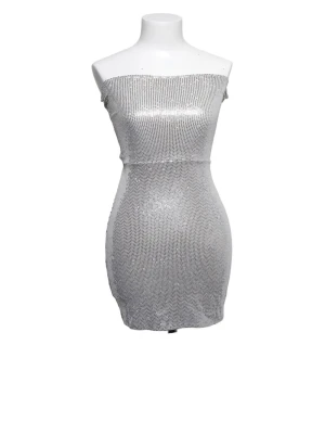 Glittrig silver axelbandslös klänning - Snygg axelbandslös kortklänning i glittrigt silvermaterial. Klänningen har en tight passform och är perfekt för dig som vill sticka ut. Materialet är syntet och ger en skimrande effekt.