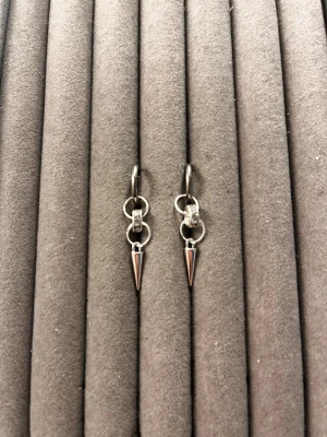 Silvriga örhängen med konformad hängare - Säljer ett par coola silvriga örhängen i ringmodell med små konformade hängen. Örhängena har en minimalistisk och edgy design, perfekta för att ge din look en extra attityd. Materialet är metall i blank finish och de har en enkel klickstängning.