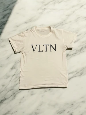 Valentino t-shirt  - Snygg vit t-shirt från Valentino med svart VLTN-tryck på bröstet. Klassisk rund halsringning och korta ärmar. Tillverkad i mjuk bomull för en bekväm känsla och clean look.