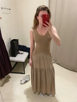 Beige långklänning med v-ringning - Aldrig använd. Inköpt i Barcelona i april. Nypris 1199kr.   Mer lik min bild i färgen än vad hemsidan visar.   Storlek XS. Jag är 167 cm. Stretchigt stickat upptill och flowy nedtill.