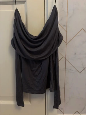 Mörkgrå offshoulder topp - Snygg mörkgrå offshoulder topp med långa ärmar. Tunn och mjuk i materialet, perfekt för en trendig look. Passar dig som gillar stilrena och unika plagg.
