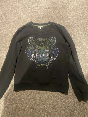 Svart sweatshirt från Kenzo - Kenzo sweatshirt i svart. Köpt i Venedig för många år sedan och säljer för att den har blivit alldeles för liten. Tröjan har inga skador och är i fint skick. Storleken är M fast för i barnstorlek.
