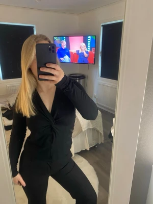 Svart omlottopp med v-ringning - Snygg svart omlottopp med v-ringning och twistad detalj framtill. Toppen har lång ärm och är figurnära i modellen, perfekt för dig som gillar en stilren och enkel look😊