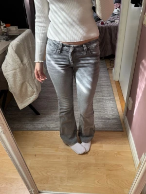 Grå bootcut jeans med fickdetaljer - Säljer ett par grå bootcut jeans med snygga fickdetaljer bak och klassisk femficksmodell. De är lowwaist, storlek 164(passar om du är runt 164cm lång) jag är 166cm och har S i byxor. Skulle säga de är xs/s. 