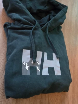 Mörkgrön hoodie från Helly Hansen - Väldigt fin hh-tröja som har en ovanlig design på bröstet och en ovanlig färg som är ljus grön, den är använd ett få tal gånger och har använt den varsamt. Priset är inte fast i sten