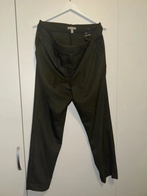 Mörkgröna kostymbyxor från H&M - Snygga mörkgröna kostymbyxor från H&M med rak passform och hög midja. Byxorna har klassisk design med pressveck och dold dragkedja fram. Tillverkade i ett mjukt och lätt material som ger en clean look.