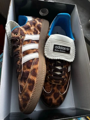 Adidas Wales Bonner leopard sneakers - Unika Adidas Wales Bonner sneakers med leopardmönstrad ovandel i pälsimitation, klassiska vita ränder på sidorna och vit plös med svart logga. Skorna har bruna snören, blå insida och gummisula. Perfekt för dig som vill sticka ut med din stil.