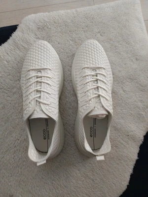 Vita sneakers från Ecco med struktur - Snygga vita sneakers från Ecco med unik strukturerad ovandel och klassisk snörning. Skorna har en låg profil och är tillverkade i ett lätt material som ger en modern look. Perfekta för dig som gillar stilrena och bekväma sneakers.