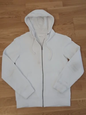 Vit zip hoodie från Pier One - Snygg vit hoodie med dragkedja framtill och huva med dragsko. Klassisk modell med ribbade muddar vid ärmslut och nederkant. Perfekt för en clean och enkel stil. Två fickor framtill för extra chill känsla.