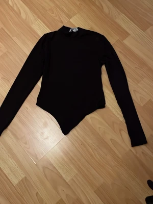 Svart långärmad body med polokrage - Snygg svart body med lång ärm och hög polokrage. Tight passform och klassisk design som passar till mycket. Tillverkad i stretchigt material för en bekväm känsla. Perfekt att styla med jeans eller kjol.