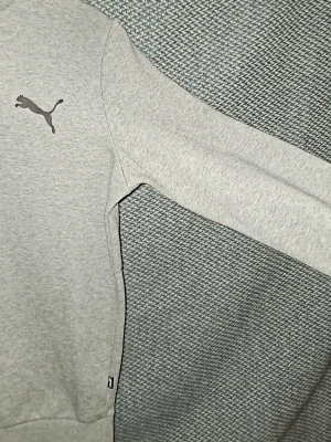 Grå sweatshirt från Puma - Snygg grå sweatshirt från Puma med klassisk rund halsringning och svart Puma-logga på bröstet. Tröjan har långa ärmar och ribbade muddar vid ärmslut och nederkant. Perfekt för en avslappnad och sportig stil. Är öppen för prisförslag vid snabb försäljning.