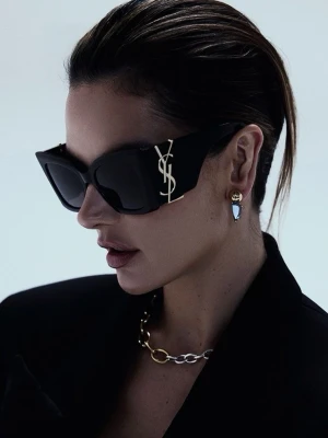 Svarta solglasögon från Saint Laurent - Säljer ett par riktigt snygga svarta solglasögon från Saint Laurent med breda bågar och ikoniska YSL-loggan i guld på sidan. Glasögonen har en kantig, trendig form och mörka linser som ger en cool och lyxig vibe.