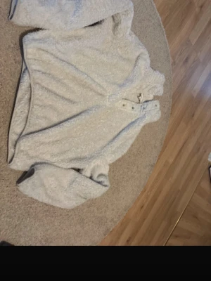 Ljusgrå teddyjacka med tryckknappar - Supermjuk och fluffig teddyjacka i ljusgrått med hög krage och tryckknappar framtill. Jackan har lång ärm och är tillverkad i ett mysigt, lurvigt material som håller dig varm. Perfekt för kyliga dagar när du vill vara både bekväm och snygg.