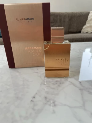 Al Haramain Amber Oud Parfym - Lyxig parfym från Al Haramain, Amber Oud, i en elegant rektangulär flaska av metall med borstad guldfinish. Kommer i en exklusiv presentförpackning med svart och guld detaljer. Doften är orientalisk och exklusiv, perfekt för dig som gillar djupa och varma toner. (Flaskan knappt använd) (75 ml)