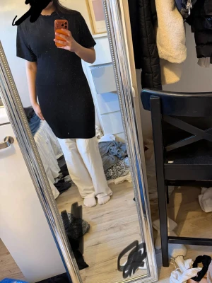 Svart klänning med kort ärm - En enkel och stilren svart klänning med korta ärmar. Modellen är rak och något loose fit, vilket gör den bekväm och lätt att styla. Perfekt att bära över jeans eller leggings. Inga synliga detaljer eller mönster.