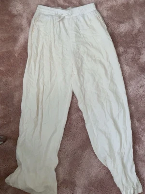 Vita linnebyxor från Vero Moda - Säljer ett par vita linnebyxor från Vero Moda med avslappnad passform och resår i midjan. Byxorna har dragsko för justerbar midja och är tillverkade i ett lätt och luftigt linnematerial. Perfekta för en chill och stilren look. dom har några fläckar som man inte ser så tydligt 💕