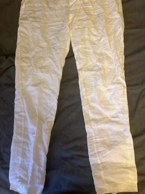 Vita linnebyxor med raka ben - Säljer ett par vita linnebyxor med raka ben och klassisk passform. Byxorna har bälteshällor, knapp och ficka bak med knappstängning. Perfekta för en avslappnad och stilren look under varma dagar.