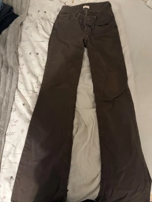 Bruna bootcut jeans med detaljer - Säljer ett par bruna bootcut jeans med snygga dekorsömmar på bakfickorna. Jeansen har klassisk femficksmodell och är tillverkade i ett mjukt bomullsmaterial. Perfekta för dig som gillar en avslappnad men trendig look. Från Nelly aldrig använda storlek 36/short passar mig som är 163.