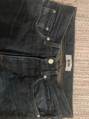 Mörkblå Acne jeans med raka ben - Snygga mörkblå jeans från Acne med klassisk femficksmodell och raka ben. Jeansen har silverfärgade nitar och knapp, samt Acne-logga på både innerlapp och bak på linningen. Tillverkade i slitstark denim, perfekta till vardagslooken. W31