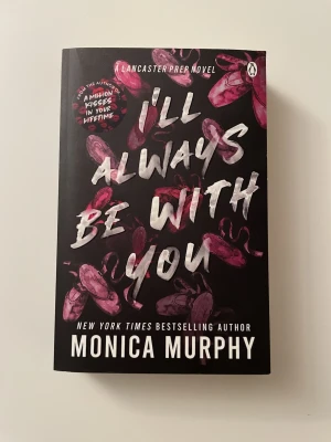 I'll Always Be With You av Monica Murphy - En svart pocketbok med titeln 'I'll Always Be With You' av Monica Murphy. Omslaget har rosa balettskor och vit text. Boken handlar om kärlek, hemligheter och relationer på en internatskola. Perfekt för dig som gillar romantiska berättelser med drama.