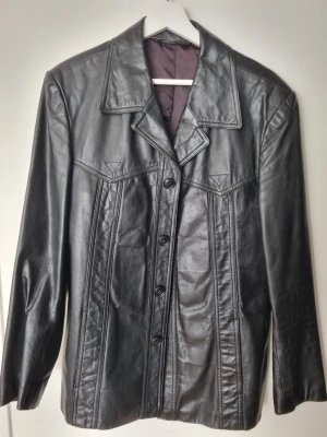 Genuine leather jacket - Black vintage leather blazer jacket with gorgeous details in perfect condition (see pictures). Great for someone who loves pockets, the jacket features 2Z zippered inner pockets, two smaller inner pockets, + and two outer pockets. bought because fell in love with the details but just never wear it, so l'm seling it on to someone who will glet better use of it! Measurements (in cm): Bust: 49 -ength: 75 Shoulders: 45 Sleeve length: 62.5
