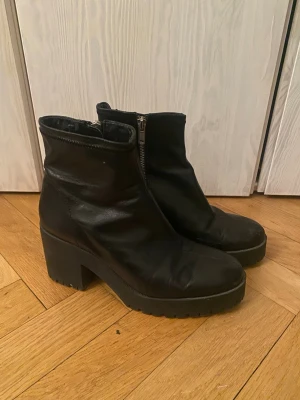 Svarta chunky stövletter med klack - Säljer ett par svarta stövletter i skinnimitation med chunky klack och grov sula från Zara. Storlek 38. Dragkedja på insidan för enkel på- och avtagning. Använda men i fint skick! Dock har tyget lossnat lite på insidan vid ankeln men inget som syns på utsidan när man bär dem. Se bild!  Snygga till fest eller vardags!