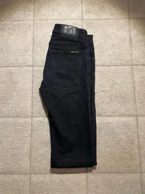Svarta jeans från Nudie Jeans - Säljer ett par svarta jeans från Nudie Jeans i modellen Skinny Lin. Jeansen har klassisk femficksdesign, smal passform och är tillverkade i stretchigt bomullsmaterial. Perfekta för dig som gillar en clean och stilren look.
