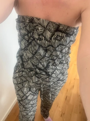Svartvit mönstrad jumpsuit Lindex - Säljer en svartvit strapless jumpsuit från Lindex i storlek S. Jumpsuiten har ett grafiskt mönster med elastisk överdel och smala ben. Tillverkad i mjukt och stretchigt material som känns skönt mot huden. Perfekt för dig som gillar en chill och trendig stil.