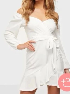 Studentklänning - Snygg vit kort omlottklänning med volangdetaljer och knyt i midjan. Klänningen har långärmade ärmar och en v-ringad hals. Perfekt för dig som vill ha en fräsch och trendig look. Endast använd 1 gång, men annars i bra skick.❤️