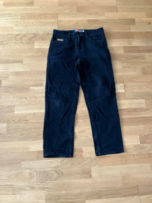 Svarta jeans från Empyre - Säljer ett par svarta jeans från Empyre med rak passform och klassisk femficksdesign. Jeansen har en liten Empyre-logga på fickan och är tillverkade i slitstarkt material, perfekta för dig som gillar en enkel och stilren look.