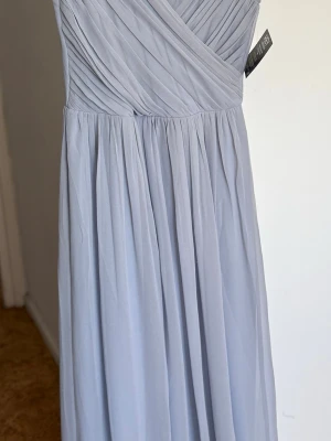 Ljuslila långklänning från Nelly - Elegant ljuslila långklänning från Nelly med omlottliv och plisserad överdel. Klänningen har ett flytande fall och är ärmlös, vilket ger en romantisk och stilren look. Tillverkad i ett tunt, mjukt tyg som ger en luftig känsla. Jag har klippt ner den.