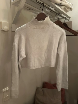 Vit croppad polotröja stickad - Säljer en vit croppad stickad polotröja med lång ärm och ribbad hög krage. Tröjan har en enkel och stilren design, perfekt för lager på lager och trendiga outfits. Materialet känns mjukt och bekvämt mot huden. Köpare står för frakt. Skriv vid frågor eller intresse 