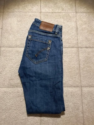 Blå dondup jeans  - Säljer ett par klassiska blå jeans från dondup Jeans med smal passform och snygga kontrastsömmar. Jeansen har fem fickor, läderpatch bak i midjan och är tillverkade i slitstark denim. Perfekta till en avslappnad stil.