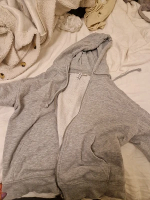Grå zip hoodie från Divided H&M - Mysig grå hoodie från Divided H&M med dragkedja framtill, två fickor och justerbar huva med snören. Tillverkad i mjuk bomullsblandning och har borstad insida för extra komfort. Perfekt för chill dagar eller när du vill ha en enkel och stilren look.