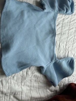 Ljusblå ribbad topp från H&M - Trendig ljusblå ribbad topp från H&M med korta puffärmar och fyrkantig urringning. Toppen är croppad och har en mjuk, stretchig passform som sitter snyggt på kroppen. Perfekt att styla med jeans eller kjol för en cool look.