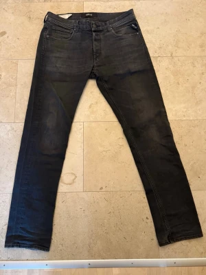 Svarta slim fit jeans från Replay - Säljer ett par svarta slim fit jeans från Replay med klassisk femficksdesign och diskreta slitningar. Jeansen har dragkedjegylf och Replay-logga vid fickan. Materialet är stretchigt denim som ger en bekväm passform.
