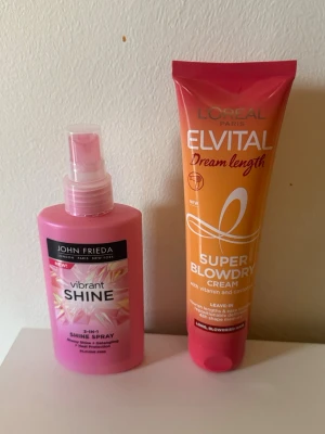 Hårvård: Shine Spray & Blowdry Cream - Man får båda för 100. Säljer två hårvårdsprodukter: John Frieda Vibrant Shine 2-in-1 Shine Spray i rosa plastflaska och L'Oréal Paris Elvital Dream Length Super Blowdry Cream i orange och rosa tub. Perfekt för dig som vill ha glansigt och lättstylat hår.