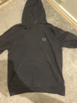 Svart Hov1 hoodie med tourtryck - Svart hoodie från Hov1 med liten krona broderad på bröstet och stort färgglatt tourtryck på ryggen med turnédatum. Klassisk känguruficka framtill och justerbar huva med snören. Perfekt för dig som gillar streetwear och vill sticka ut.